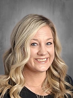 Smiling woman with long, wavy blonde hair, wearing a black top, against a gray background.
