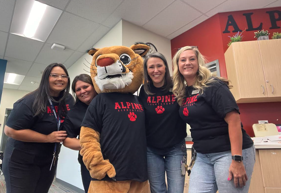 Four women and a mascot in a classroom, all wearing matching black shirts with "Alpine Elementary" printed on them.