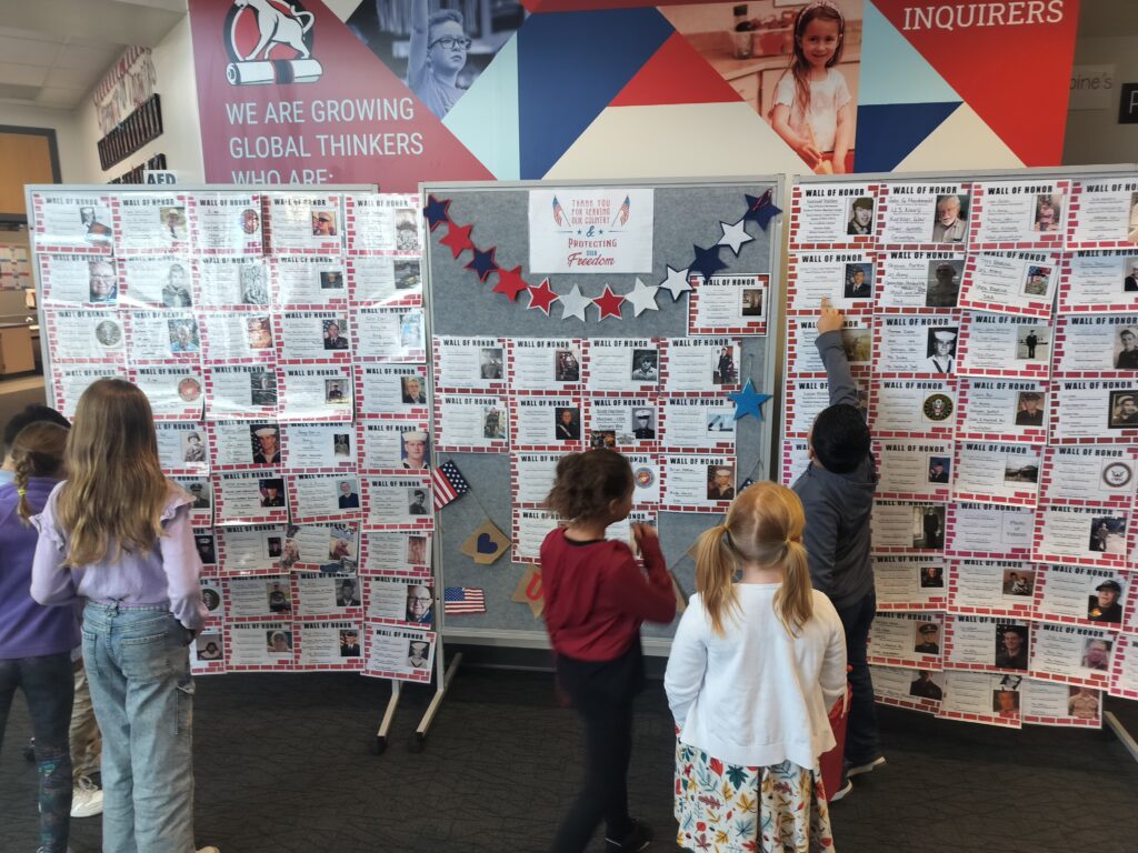 Students observe a "Wall of Honor" display featuring photos and information about various individuals.