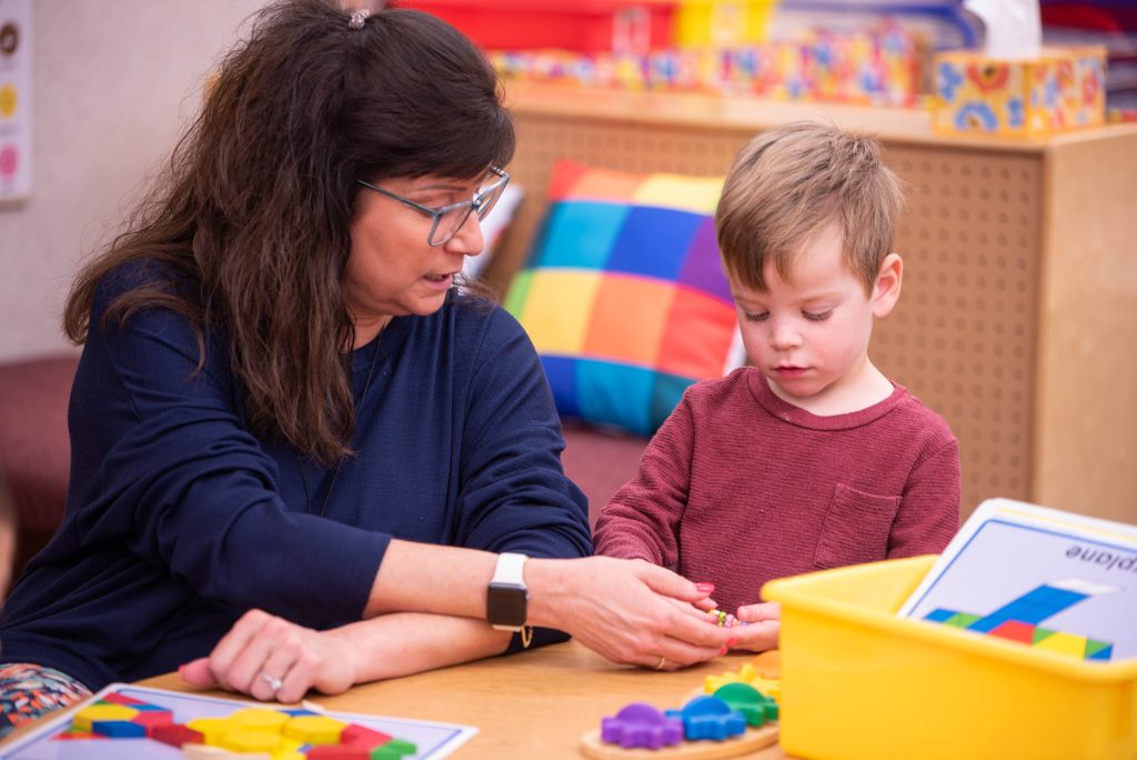 A child and an adult engage in a hands-on activity with colorful geometric shapes on a table.